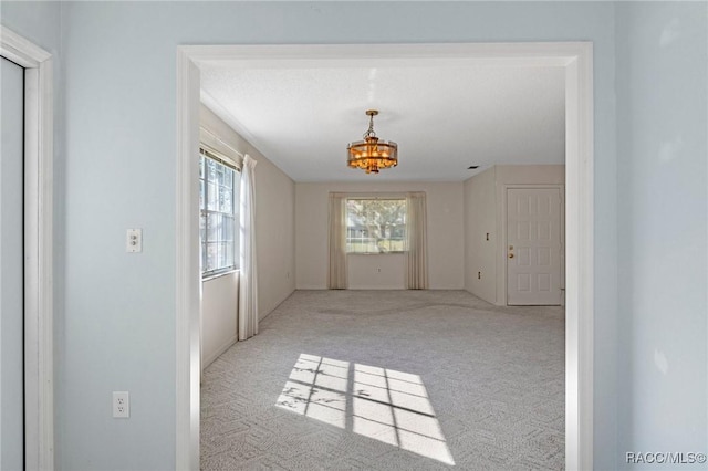 carpeted empty room with an inviting chandelier