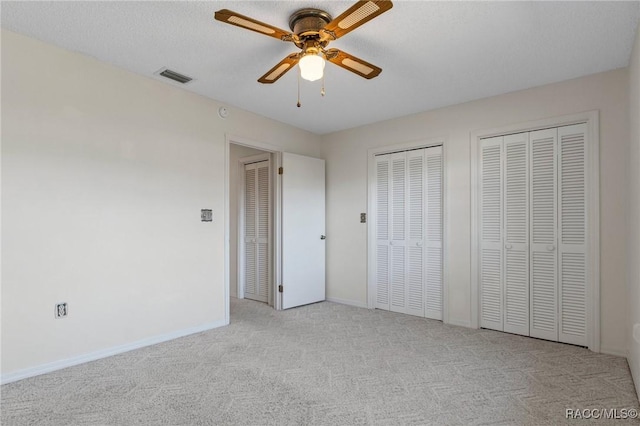 unfurnished bedroom with ceiling fan, two closets, light colored carpet, and a textured ceiling