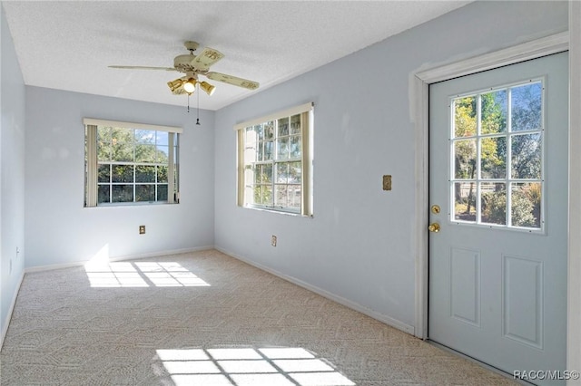 doorway featuring a textured ceiling, ceiling fan, a wealth of natural light, and carpet