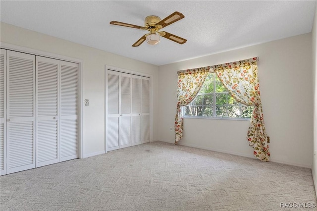 unfurnished bedroom featuring light carpet, multiple closets, ceiling fan, and a textured ceiling