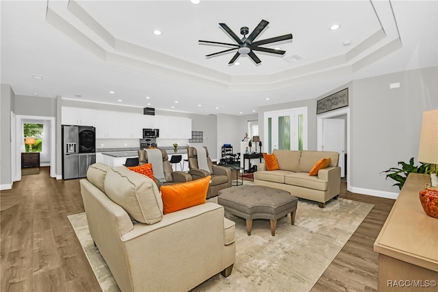 living room with light hardwood / wood-style floors, a raised ceiling, and ceiling fan