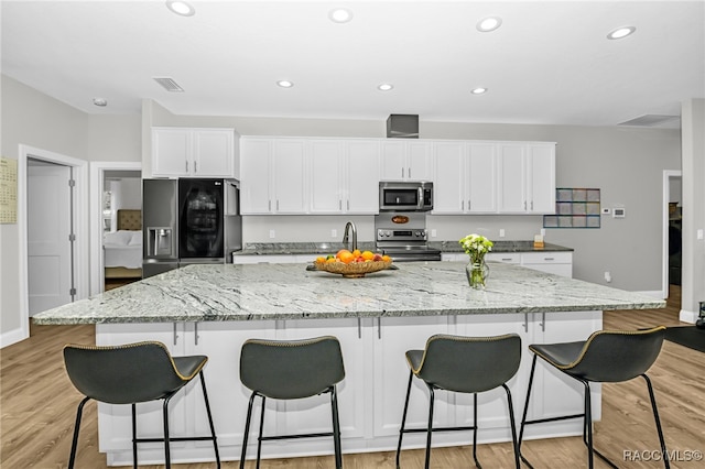 kitchen featuring stainless steel appliances, light stone counters, light hardwood / wood-style flooring, a spacious island, and white cabinets