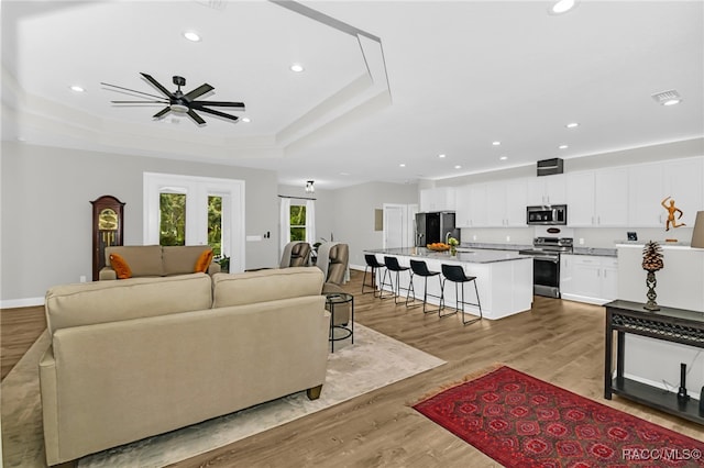 living room with a tray ceiling, ceiling fan, and light wood-type flooring