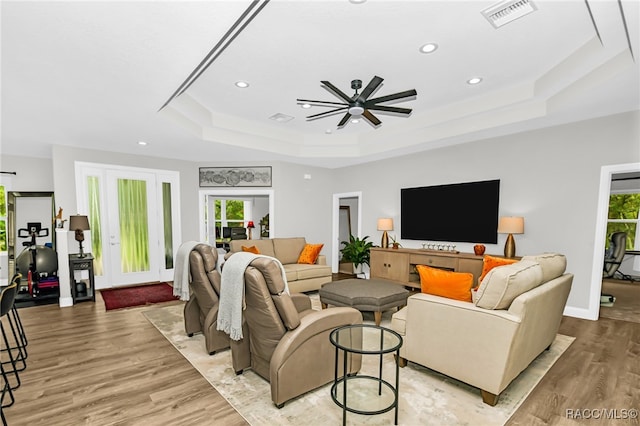 living room with light hardwood / wood-style floors, a raised ceiling, ceiling fan, and a healthy amount of sunlight