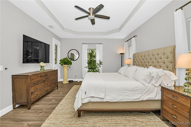 bedroom with access to exterior, dark hardwood / wood-style flooring, a raised ceiling, and ceiling fan