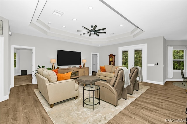 living room with ceiling fan, light hardwood / wood-style floors, french doors, and a tray ceiling