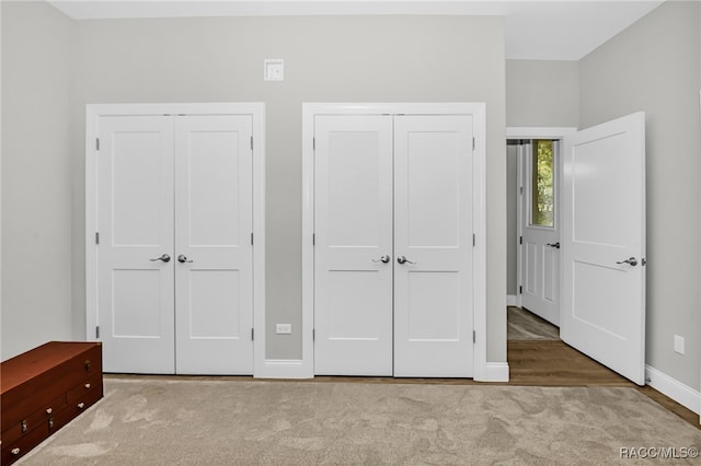 unfurnished bedroom featuring light colored carpet and multiple closets