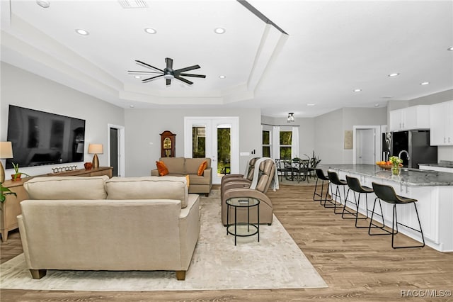 living room featuring ceiling fan, a raised ceiling, french doors, and light hardwood / wood-style flooring