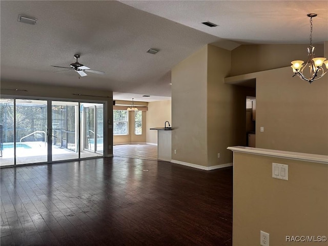 unfurnished living room featuring ceiling fan with notable chandelier, vaulted ceiling, dark wood-type flooring, and a healthy amount of sunlight