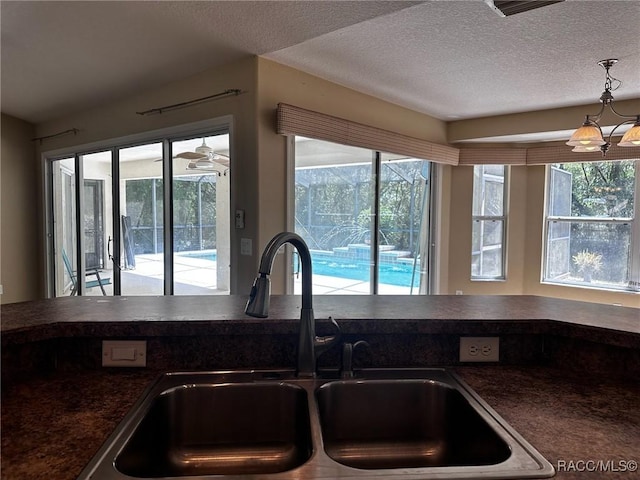 kitchen with a sink, a textured ceiling, dark countertops, a notable chandelier, and decorative light fixtures