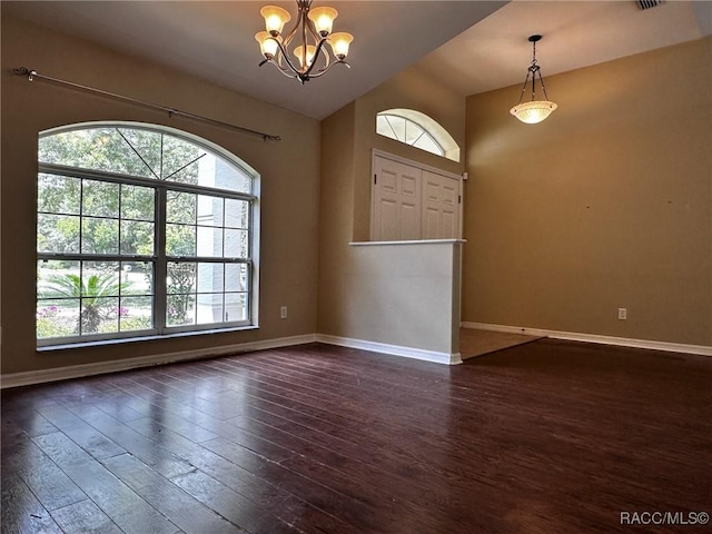 spare room featuring dark wood-type flooring, vaulted ceiling, baseboards, and a notable chandelier