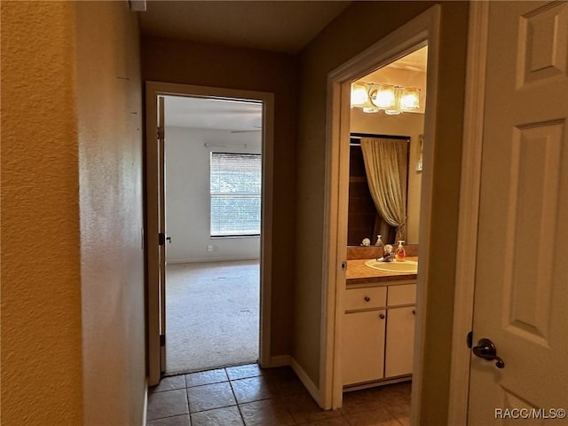 corridor with light carpet, baseboards, a sink, and light tile patterned floors