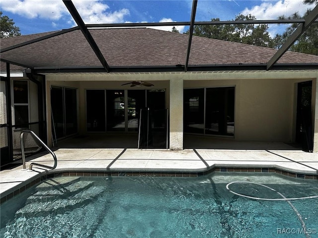 outdoor pool with glass enclosure, a patio area, and a ceiling fan