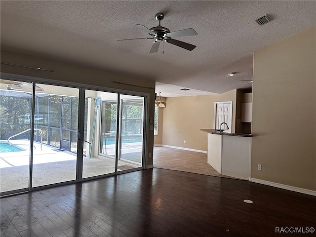unfurnished living room featuring a ceiling fan, wood finished floors, a textured ceiling, baseboards, and visible vents