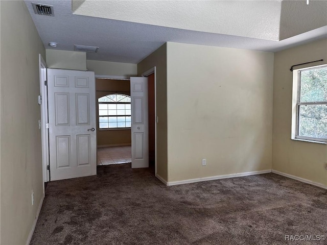 unfurnished room featuring a wealth of natural light, a textured ceiling, and carpet