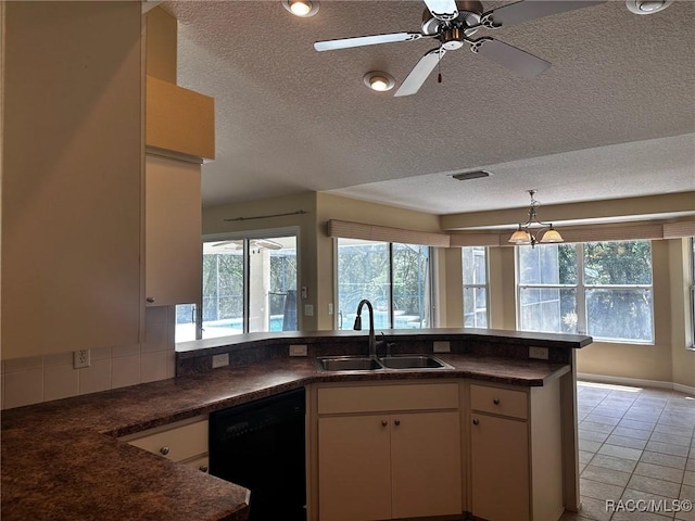 kitchen featuring dark countertops, a sink, a textured ceiling, dishwasher, and visible vents