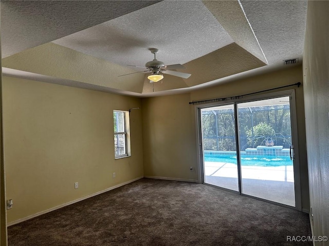 carpeted empty room with a raised ceiling, visible vents, baseboards, a textured ceiling, and ceiling fan