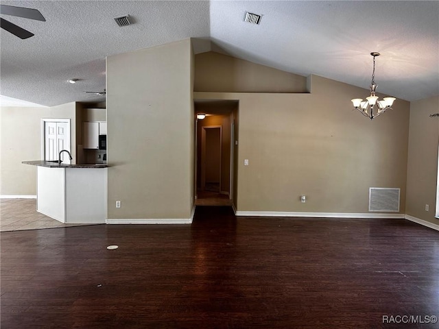 unfurnished living room featuring vaulted ceiling, visible vents, wood finished floors, and ceiling fan with notable chandelier