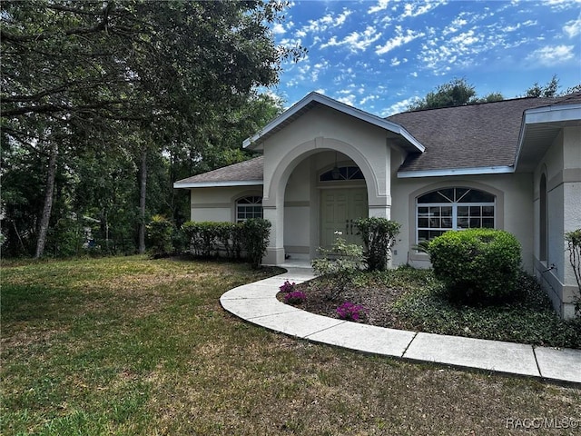 doorway to property with stucco siding, roof with shingles, and a lawn
