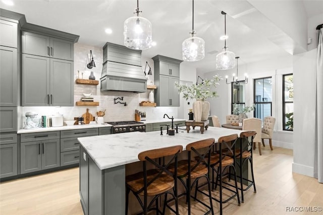 kitchen featuring gray cabinetry, a kitchen island with sink, a kitchen breakfast bar, and premium range hood