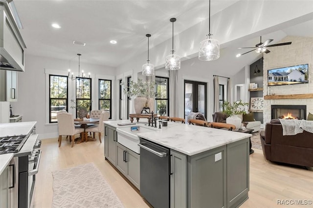 kitchen with pendant lighting, appliances with stainless steel finishes, gray cabinets, vaulted ceiling, and a center island with sink