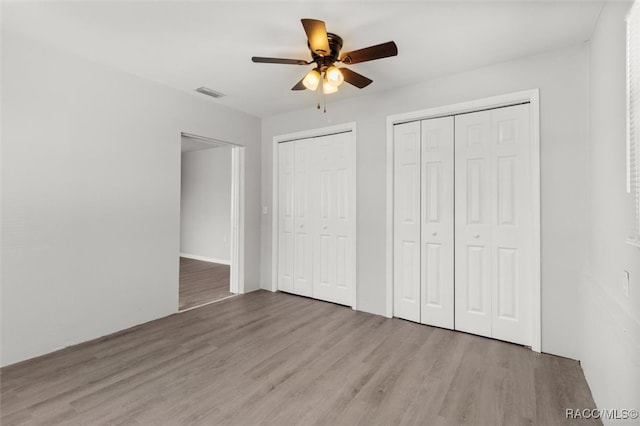 unfurnished bedroom with multiple closets, ceiling fan, and light hardwood / wood-style flooring