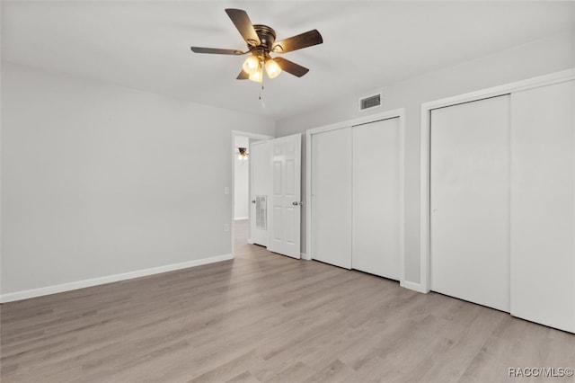 unfurnished bedroom featuring two closets, light hardwood / wood-style floors, and ceiling fan