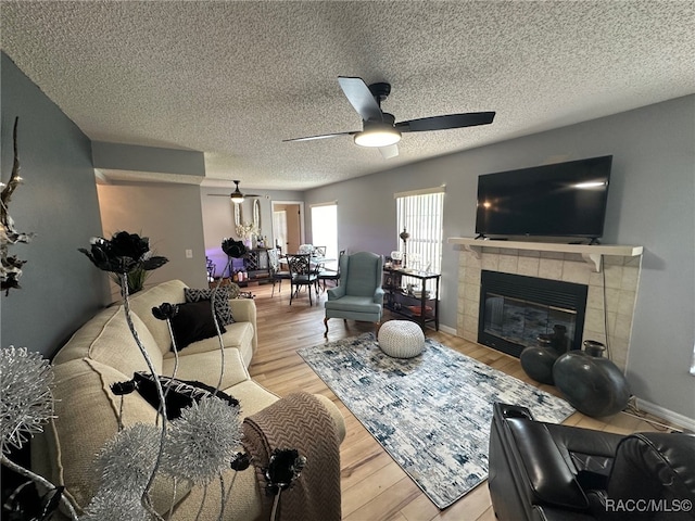 living room featuring ceiling fan, a textured ceiling, a fireplace, and light hardwood / wood-style floors