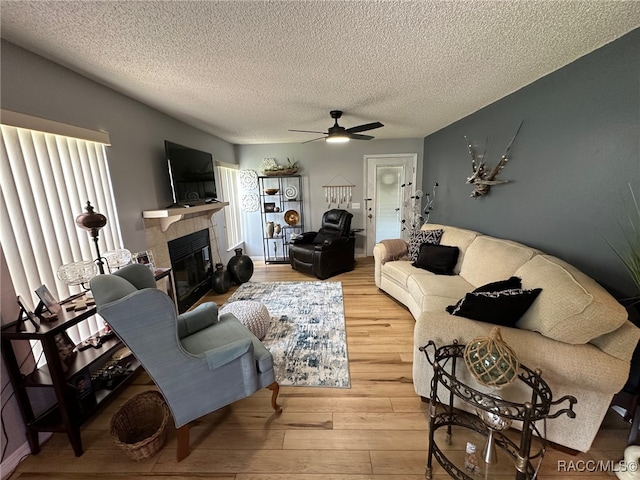 living room with hardwood / wood-style flooring, a tile fireplace, ceiling fan, and a textured ceiling