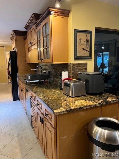 kitchen featuring black fridge, decorative backsplash, light tile patterned floors, and dark stone counters