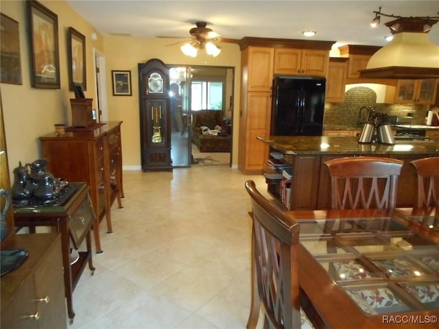 kitchen featuring premium range hood, dark stone counters, black refrigerator, ceiling fan, and tasteful backsplash