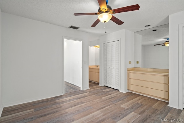 unfurnished bedroom with connected bathroom, ceiling fan, a textured ceiling, and hardwood / wood-style flooring