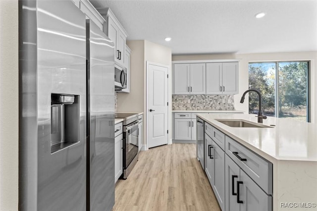 kitchen featuring light countertops, decorative backsplash, appliances with stainless steel finishes, a sink, and light wood-type flooring