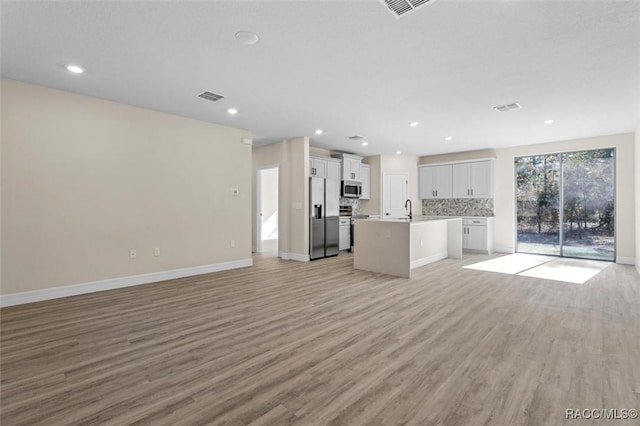 unfurnished living room with light wood-style floors, baseboards, visible vents, and a sink