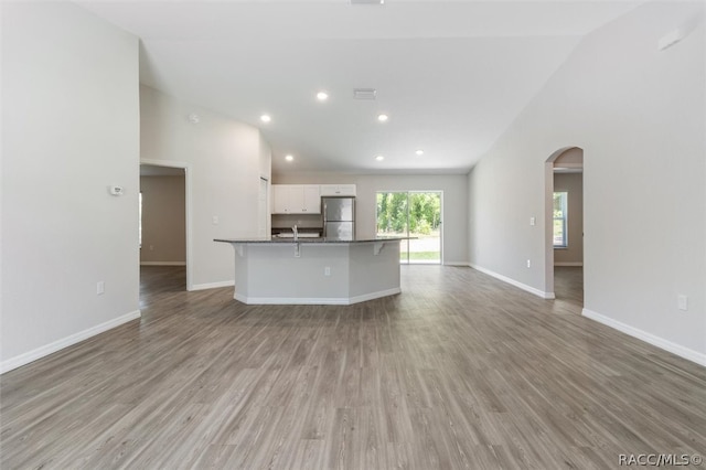 kitchen with stainless steel fridge, a breakfast bar, a center island with sink, white cabinets, and light hardwood / wood-style floors