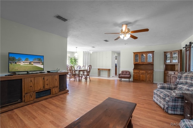 living room with ceiling fan, a barn door, light wood-type flooring, and a textured ceiling