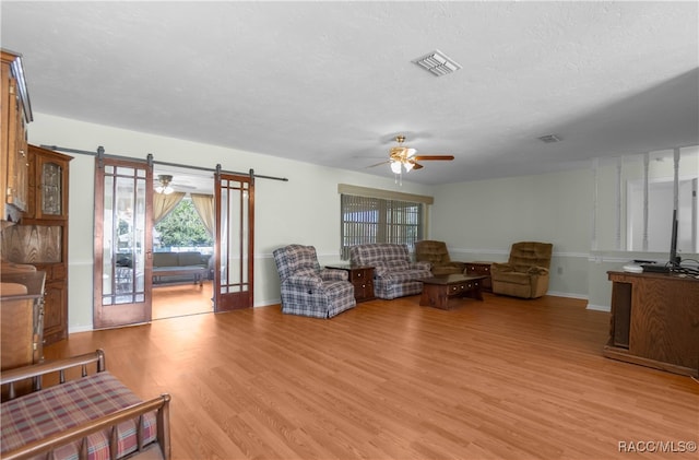 living room with ceiling fan, light hardwood / wood-style floors, a textured ceiling, and french doors