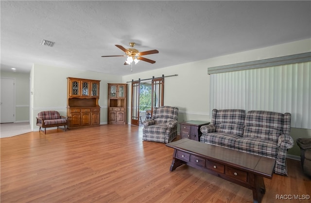 living room featuring ceiling fan, light hardwood / wood-style flooring, and a textured ceiling