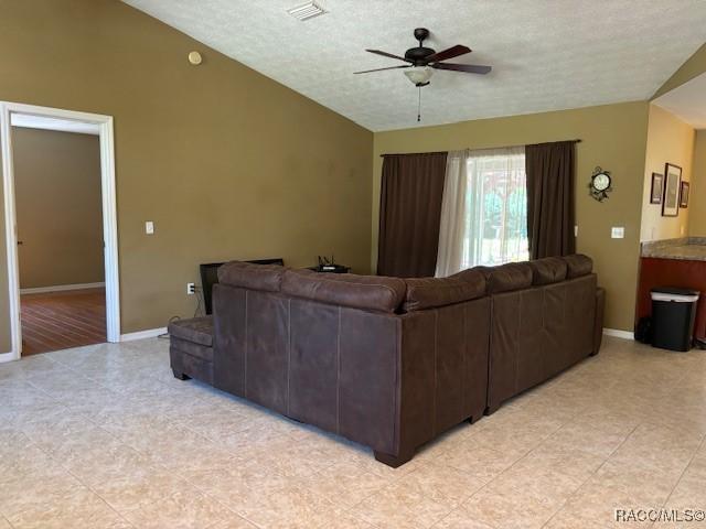 living room with light tile patterned floors, a textured ceiling, a ceiling fan, visible vents, and baseboards