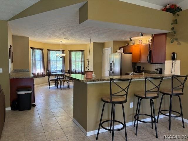 kitchen with a peninsula, brown cabinets, a kitchen breakfast bar, and stainless steel refrigerator with ice dispenser