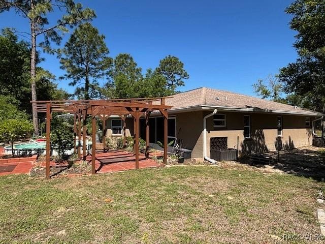 rear view of property with a pergola, a patio area, stucco siding, and a lawn