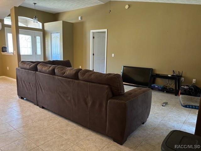 living area featuring light tile patterned floors, baseboards, and lofted ceiling