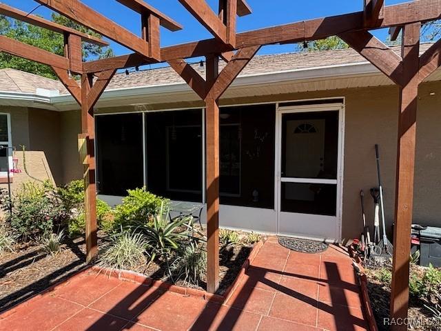 property entrance featuring a patio area, stucco siding, and roof with shingles
