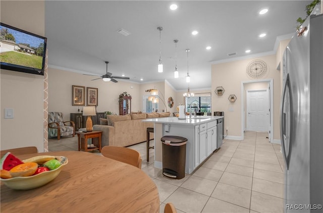 kitchen featuring pendant lighting, white cabinetry, ornamental molding, stainless steel appliances, and a center island with sink