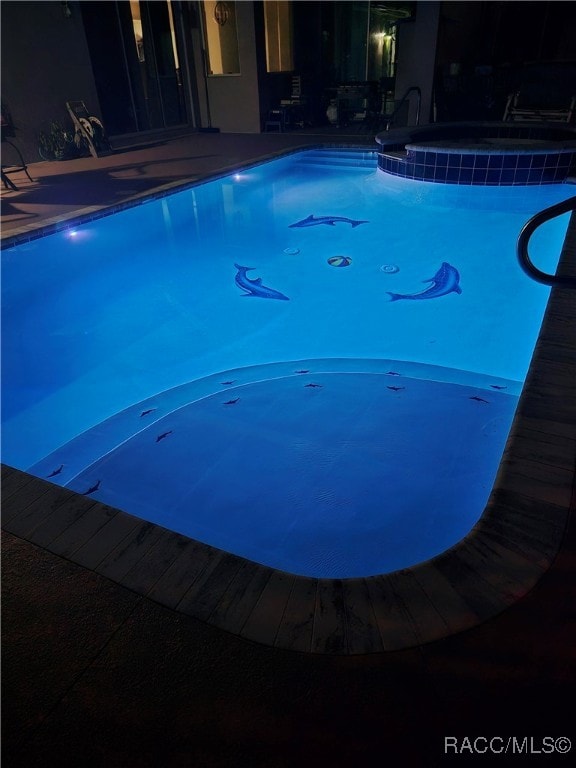 pool at twilight featuring an in ground hot tub and a patio