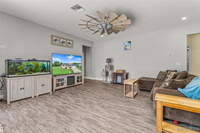 living room with ceiling fan, light wood-type flooring, and a textured ceiling