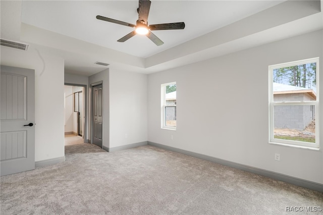 spare room with ceiling fan, a tray ceiling, and light carpet