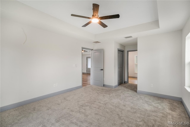 unfurnished bedroom featuring ceiling fan, light carpet, and a tray ceiling