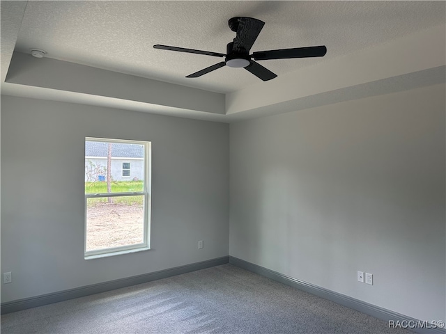 empty room with a raised ceiling, ceiling fan, carpet, and a textured ceiling