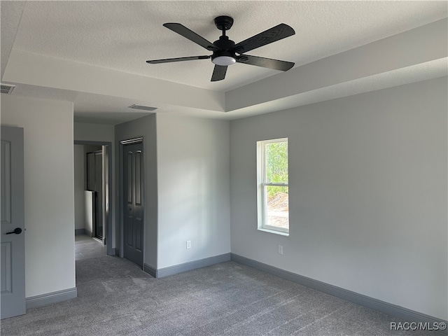 spare room featuring a textured ceiling, ceiling fan, carpet, and a raised ceiling